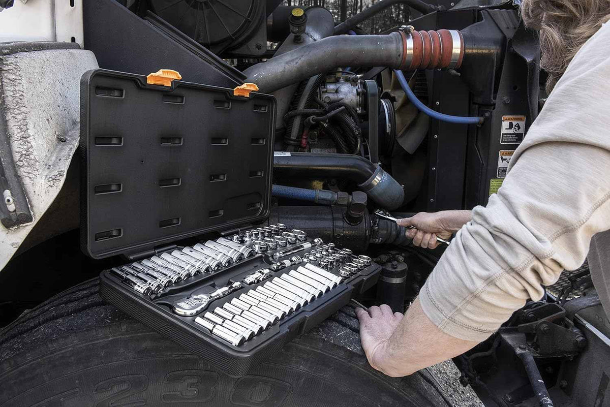 A professional using the GearWrench 80550 57-piece socket set on a job site with the blow-molded case resting on a heavy-duty vehicle tire for easy tool access.