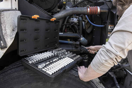 A professional using the GearWrench 80550 57-piece socket set on a job site with the blow-molded case resting on a heavy-duty vehicle tire for easy tool access.