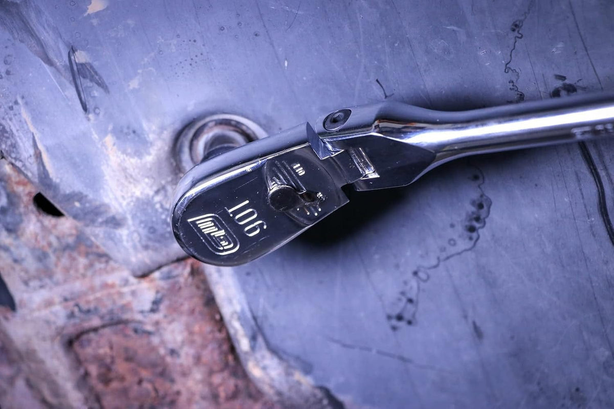 A close-up macro shot of the 90-tooth flex head on a GEARWRENCH ratchet, shown on a dark, rusty metal surface.