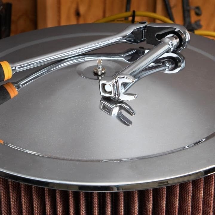 Artistic shot of two ratchet wrenches with extensions and crowfoot wrenches resting on a chrome engine air filter cover.