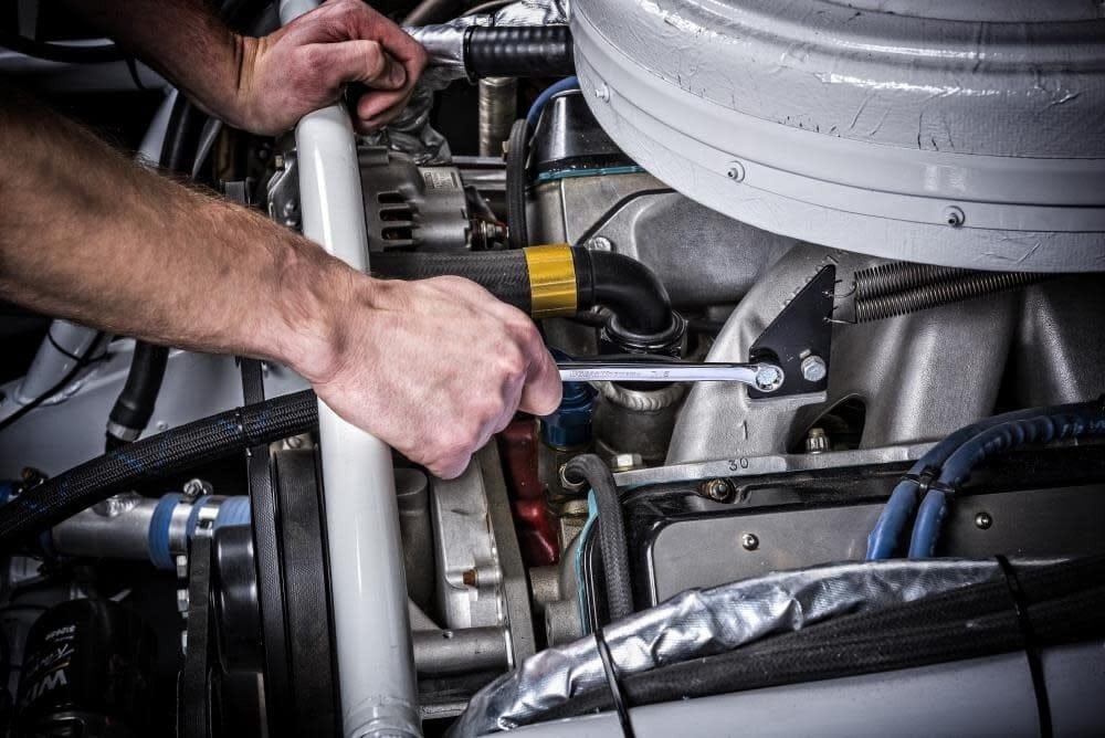 Action shot of a mechanic using the long pattern wrench to access a bolt within a crowded vehicle engine bay.