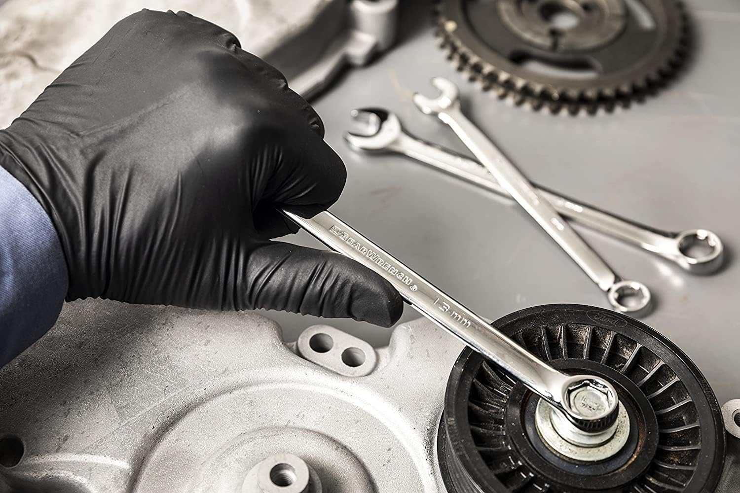 Action shot of a mechanic's gloved hand holding a polished chrome combination wrench against an engine pulley.