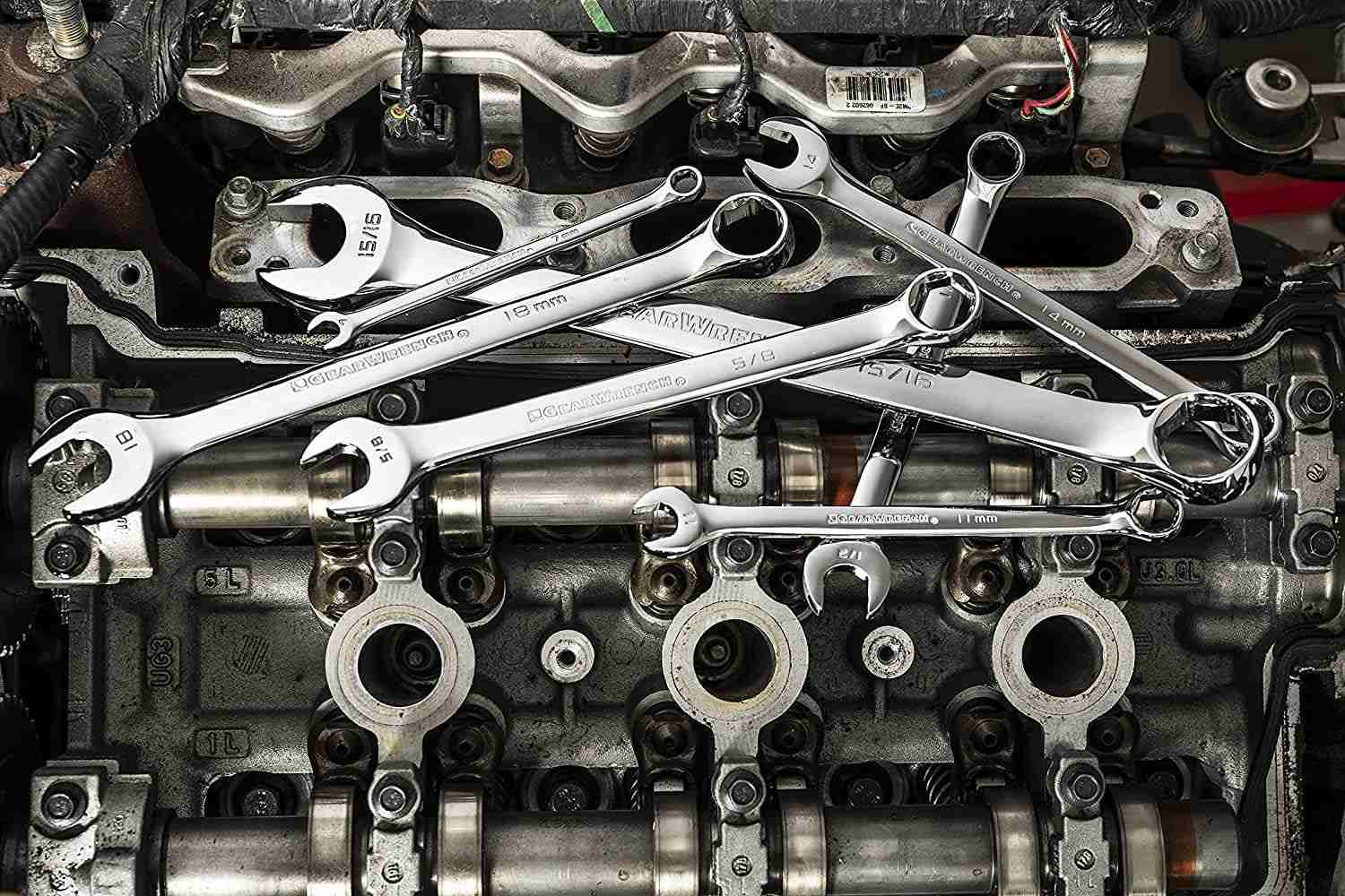 Artistic arrangement of various combination wrenches resting on top of a metallic engine valve cover.