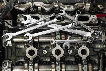 Artistic arrangement of various combination wrenches resting on top of a metallic engine valve cover.