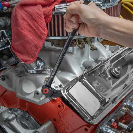 Action shot of a mechanic using the indexing pry bar to lift a chrome valve cover on an engine.