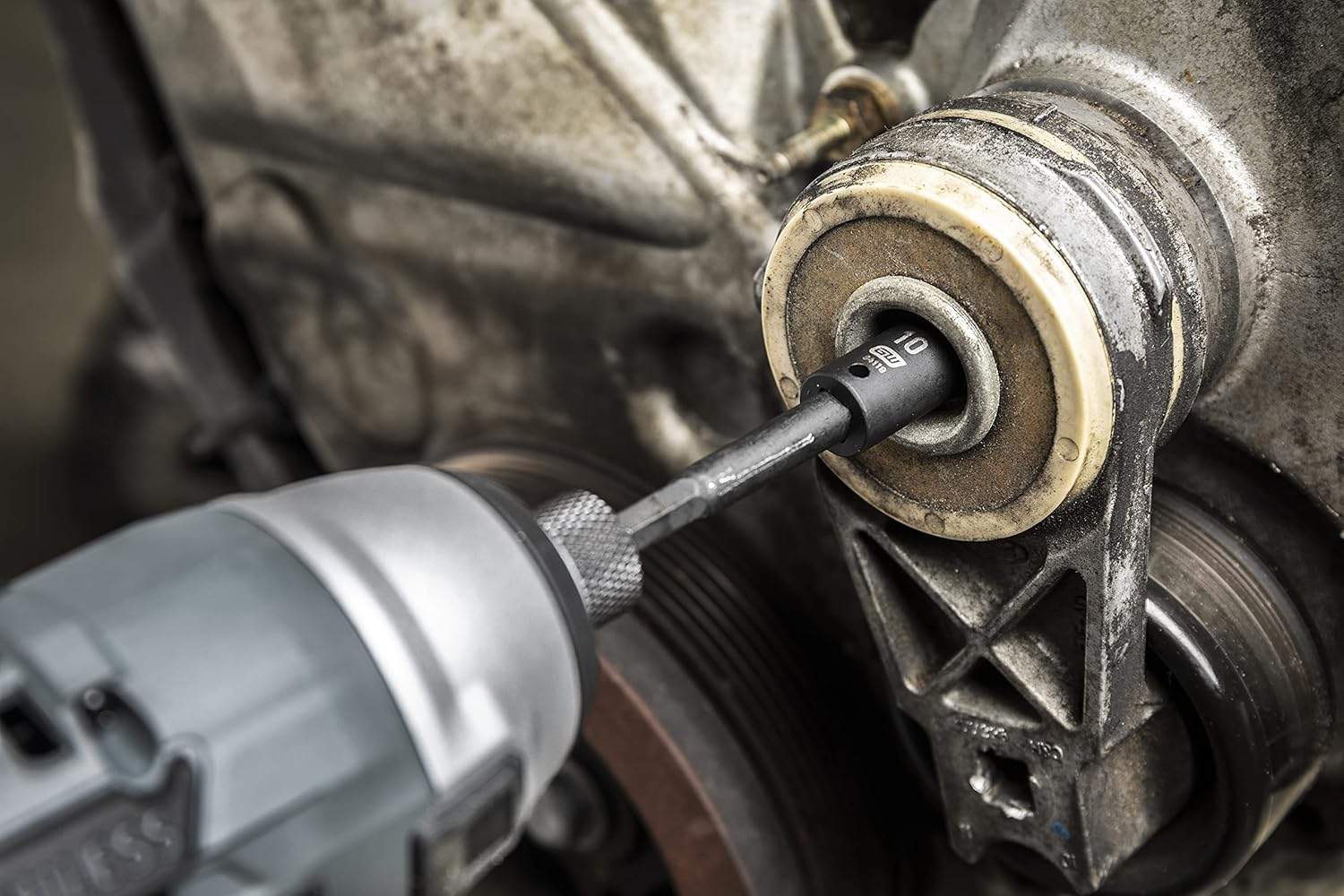 Close-up action shot of a cordless impact driver using a GearWrench impact socket to tighten a bolt on a vehicle belt tensioner.