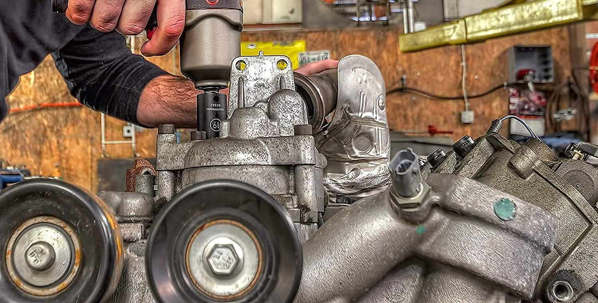 Person using a power tool on a mechanical engine component in a workshop, surrounded by pulleys and metal casings.