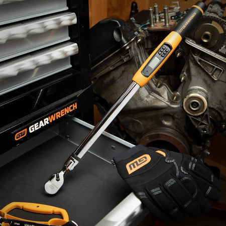 GearWrench digital torque wrench with display and buttons shown on a workbench beside gloves and engine block.