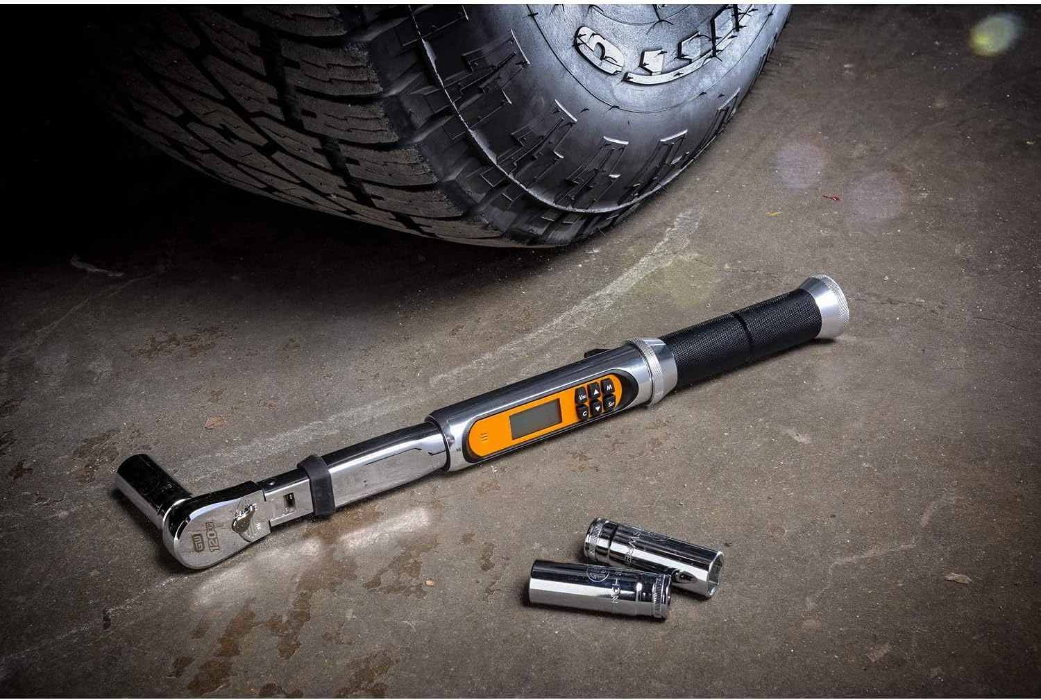 The GEARWRENCH 1/4-inch electronic torque wrench with a socket attached, resting on a concrete garage floor next to a tire.