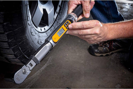 An action shot of a person's hands adjusting the settings on the digital display of the GEARWRENCH electronic torque wrench next to a car wheel.