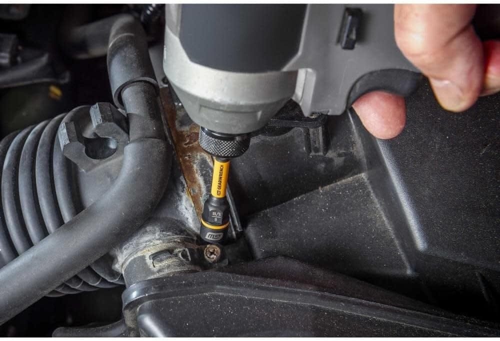 A high-access application shot of the 86187 Bolt Biter being used with a power tool to extract a stripped bolt within a cramped engine bay, showcasing its slim profile and industrial versatility.