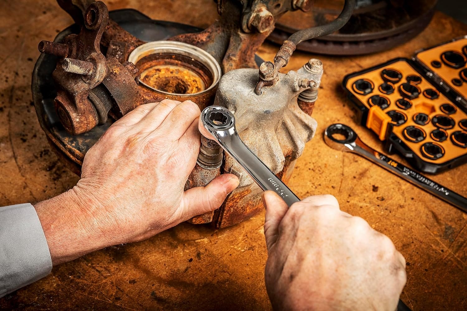Action shot demonstrating a GearWrench Bolt Biter insert being used with a ratcheting wrench to remove a heavily rusted and damaged bolt from a vehicle's suspension component.