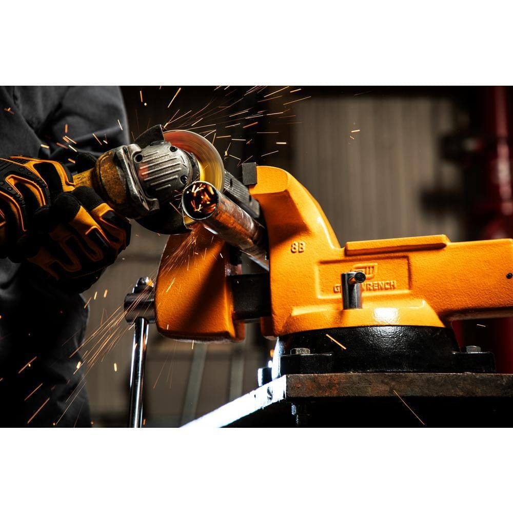 A worker using an angle grinder to cut a metal pipe secured in the pipe jaws of the GearWrench GWBVA8 bench vise, demonstrating its high clamping force and stability.