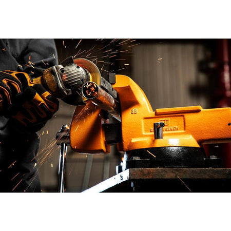 A worker using an angle grinder to cut a metal pipe secured in the pipe jaws of the GearWrench GWBVA8 bench vise, demonstrating its high clamping force and stability.