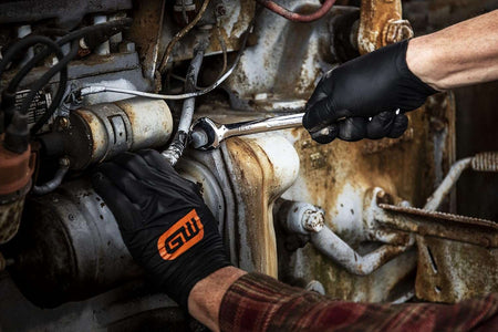 Close-up of a professional mechanic using a GearWrench combination wrench to service a large vehicle engine, demonstrating precision and speed.