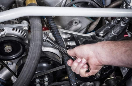 Action shot of a mechanic's hand using a GearWrench ratcheting wrench to tighten a bolt in a crowded engine compartment.