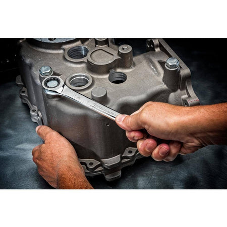 Action shot of a mechanic's hand using a GearWrench ratcheting wrench to tighten a bolt on a metal engine casing.
