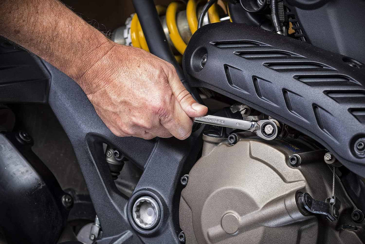 Action shot of a mechanic's hand using the reversible ratcheting wrench to tighten a bolt on the side of a motorcycle engine case.