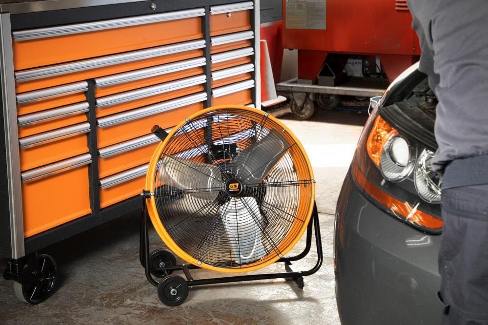 GearWrench high-velocity shop fan placed beside a mechanic's tool cabinet and vehicle to circulate cooling airflow.