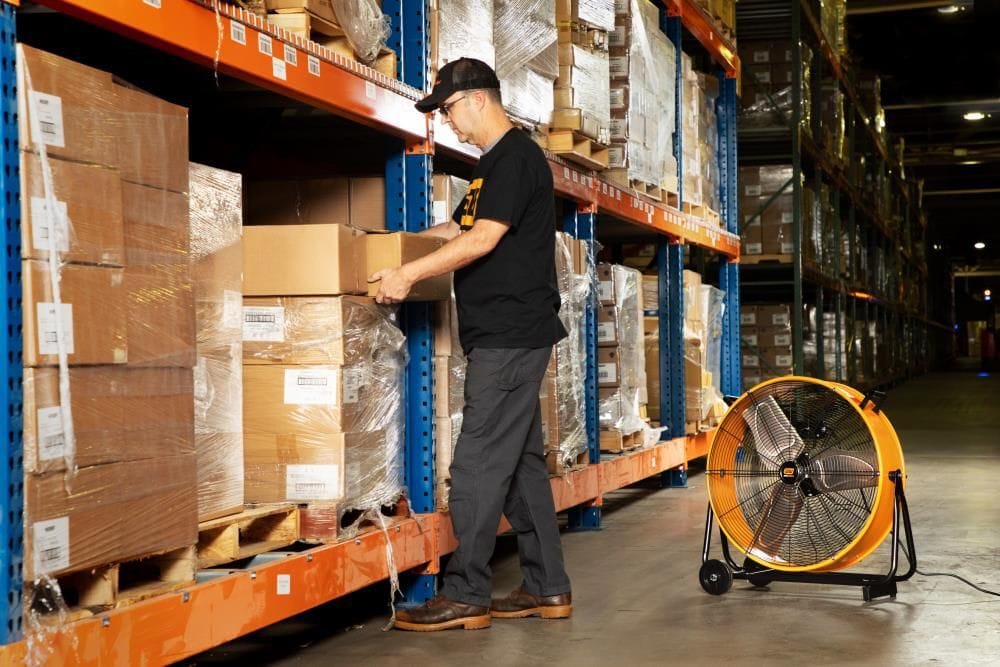 Warehouse employee working in a storage aisle with the GearWrench 24-inch industrial fan providing active ventilation.