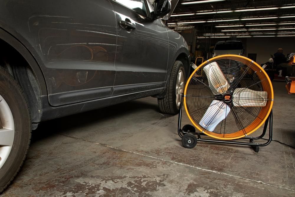 Low-angle view of the GearWrench 24-inch high-velocity fan running beside an SUV in an auto repair shop.