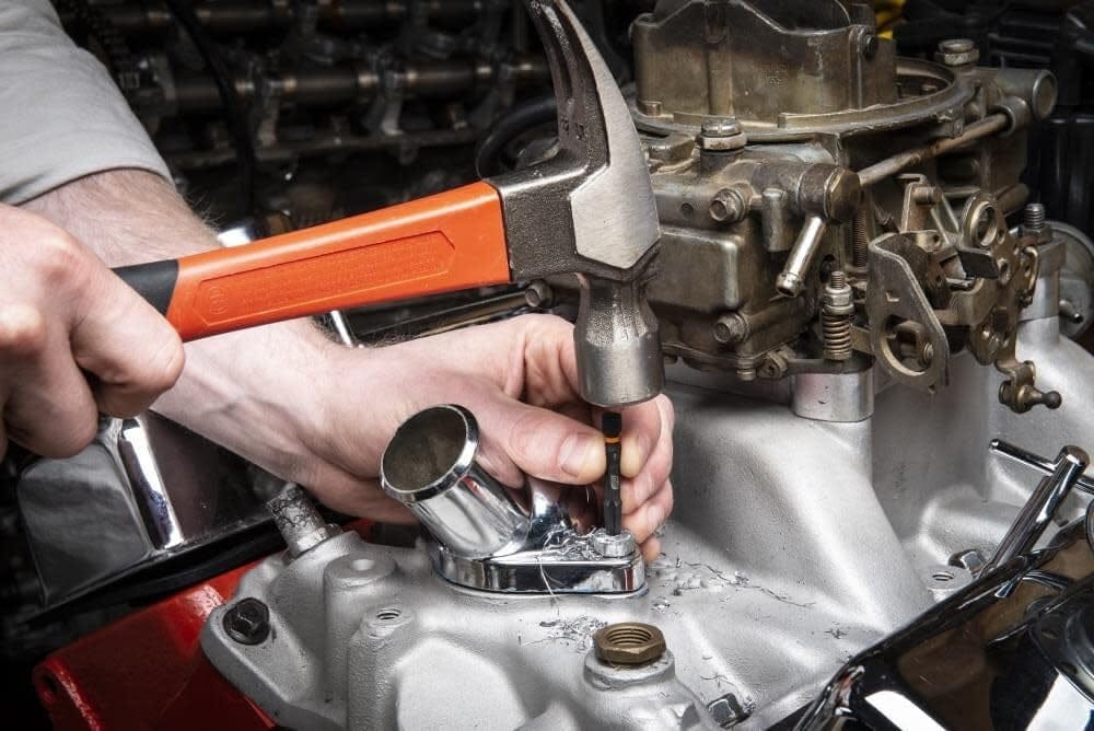 An action shot of a mechanic tapping a Bolt Biter extractor with a hammer into a broken bolt on a vehicle's engine block.