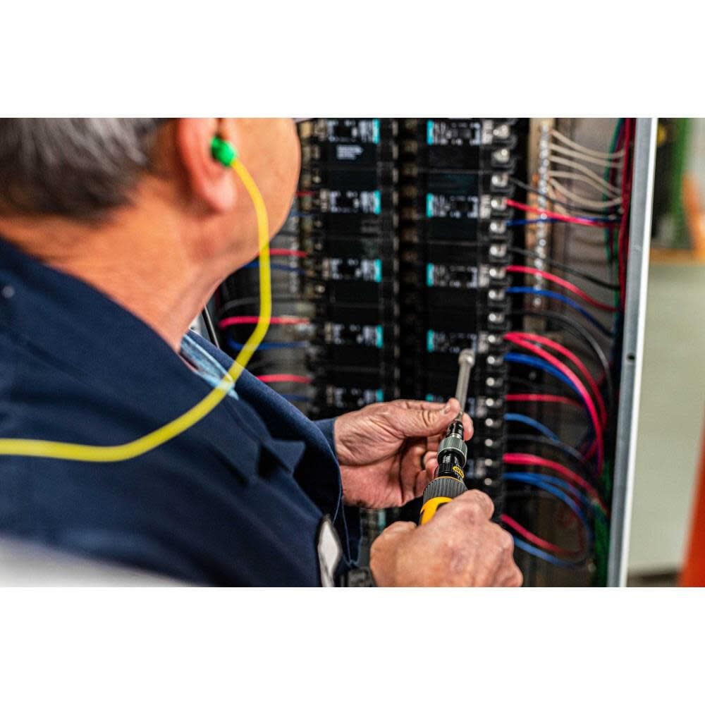 Close-up action shot of an electrician wearing safety earplugs using the Gearwrench torque screwdriver with a long nut driver bit to secure connections inside a high-voltage electrical breaker panel.