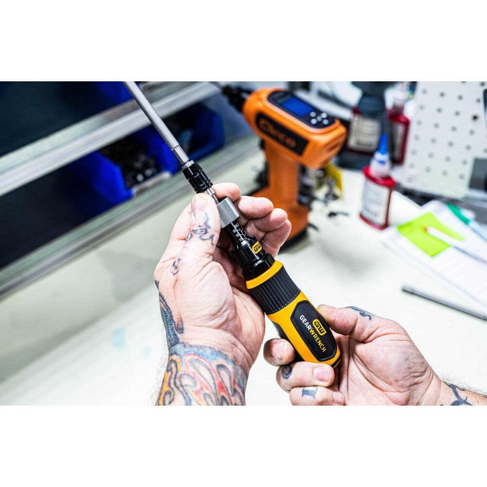 A technician with tattooed arms holding the Gearwrench torque screwdriver vertically to inspect the locking adjustment collar and quick-release bit holder during a professional tool setup.