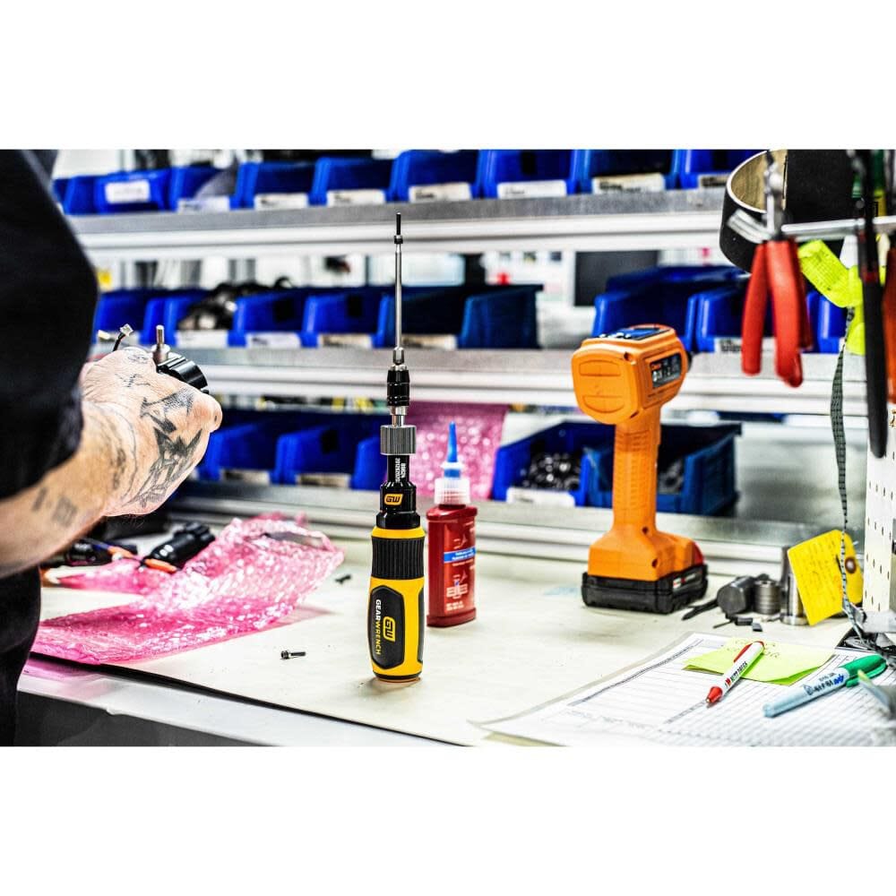 The Gearwrench torque screwdriver standing upright on a cluttered industrial workbench next to assembly parts and fluid containers, showcasing its durable, solvent-resistant handle design.