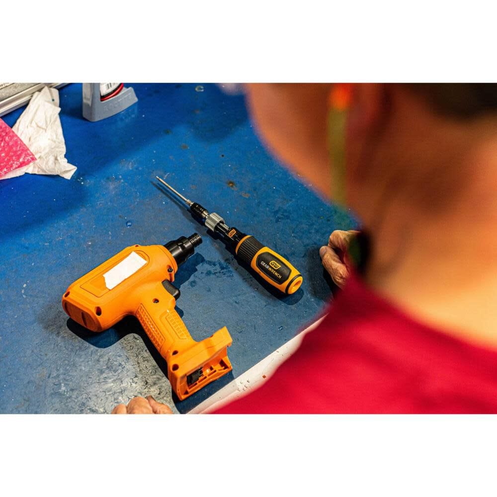 Over-the-shoulder view of a professional using the Gearwrench torque screwdriver alongside an orange cordless power tool, illustrating its role as a essential precision instrument for sensitive fastening tasks.