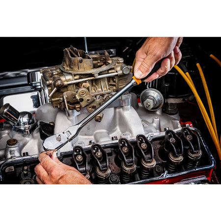 An overhead perspective view of a mechanic utilizing the 17-inch long reach handle and flexible pivoting mechanism of the Gearwrench 1/2-inch drive ratchet to adjust valvetrain components inside a complex automotive engine block.