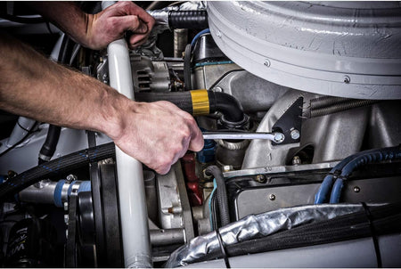 Close-up action shot of a mechanic using a Gearwrench long pattern metric combination spanner to tighten a fastener directly inside a high-density, complex automotive engine bay.