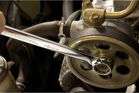 Detailed workshop view showing a polished chrome 19mm Gearwrench spanner being applied to a central pulley bolt mechanism on a vehicle motor engine assembly.