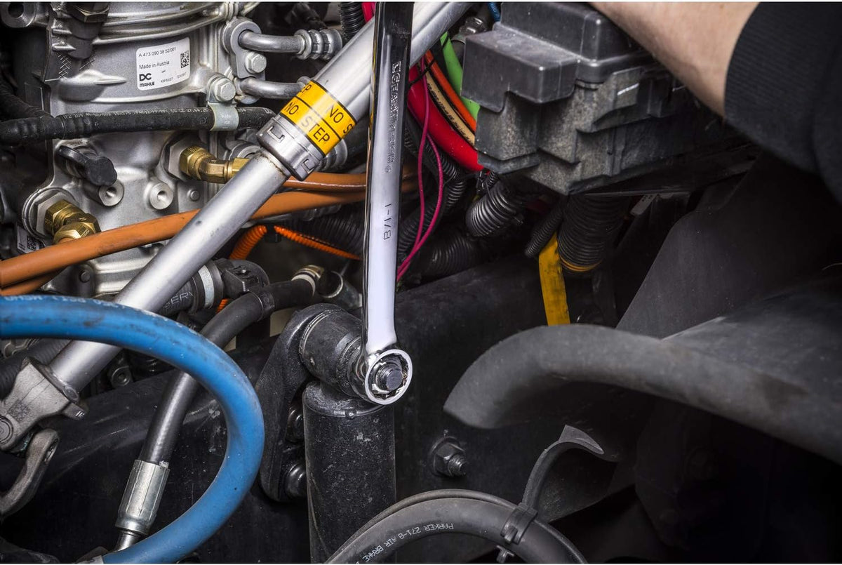 Industrial mechanical view showing a full-polish chrome Gearwrench combination wrench engaged with a heavy-duty structural mount hex bolt inside a complex commercial vehicle engine compartment.