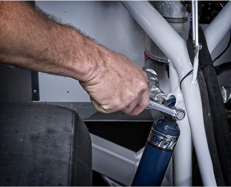 Close-up action view of a hand applying leverage with a 12-point closed box end Gearwrench combination spanner onto a performance shock absorber mounting bolt within a custom automotive chassis frame.