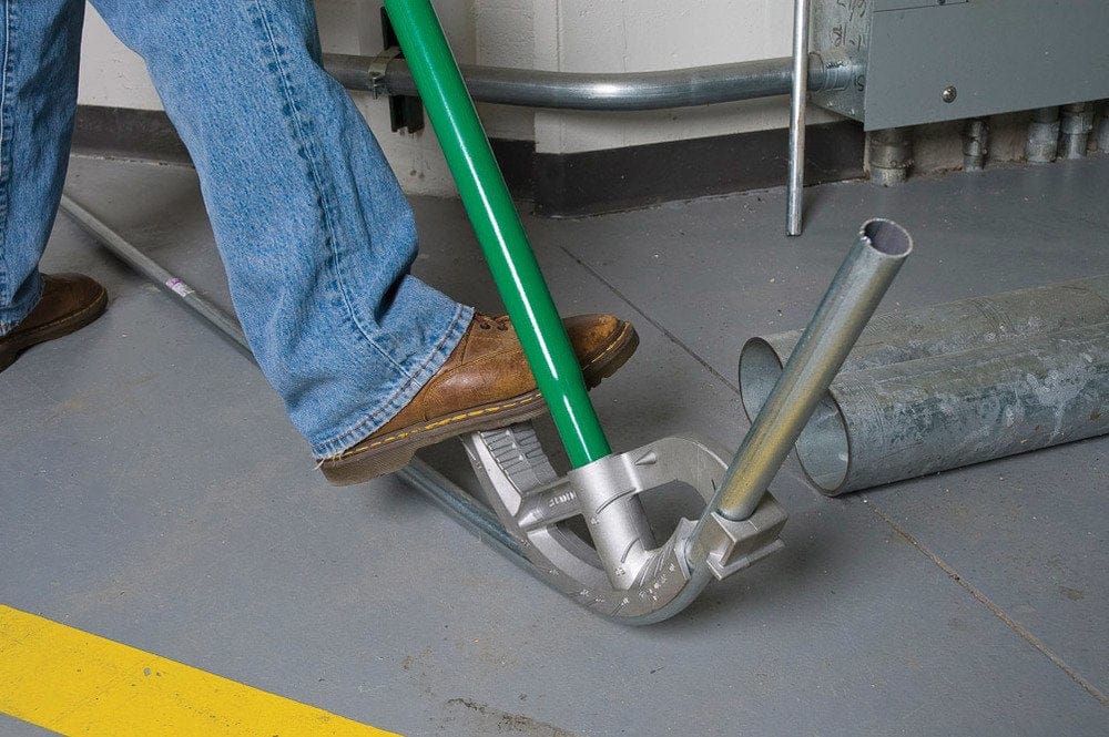 Close-up action view of a user's foot applying pressure to the bender's enlarged foot pedal to leverage a bend in the conduit.