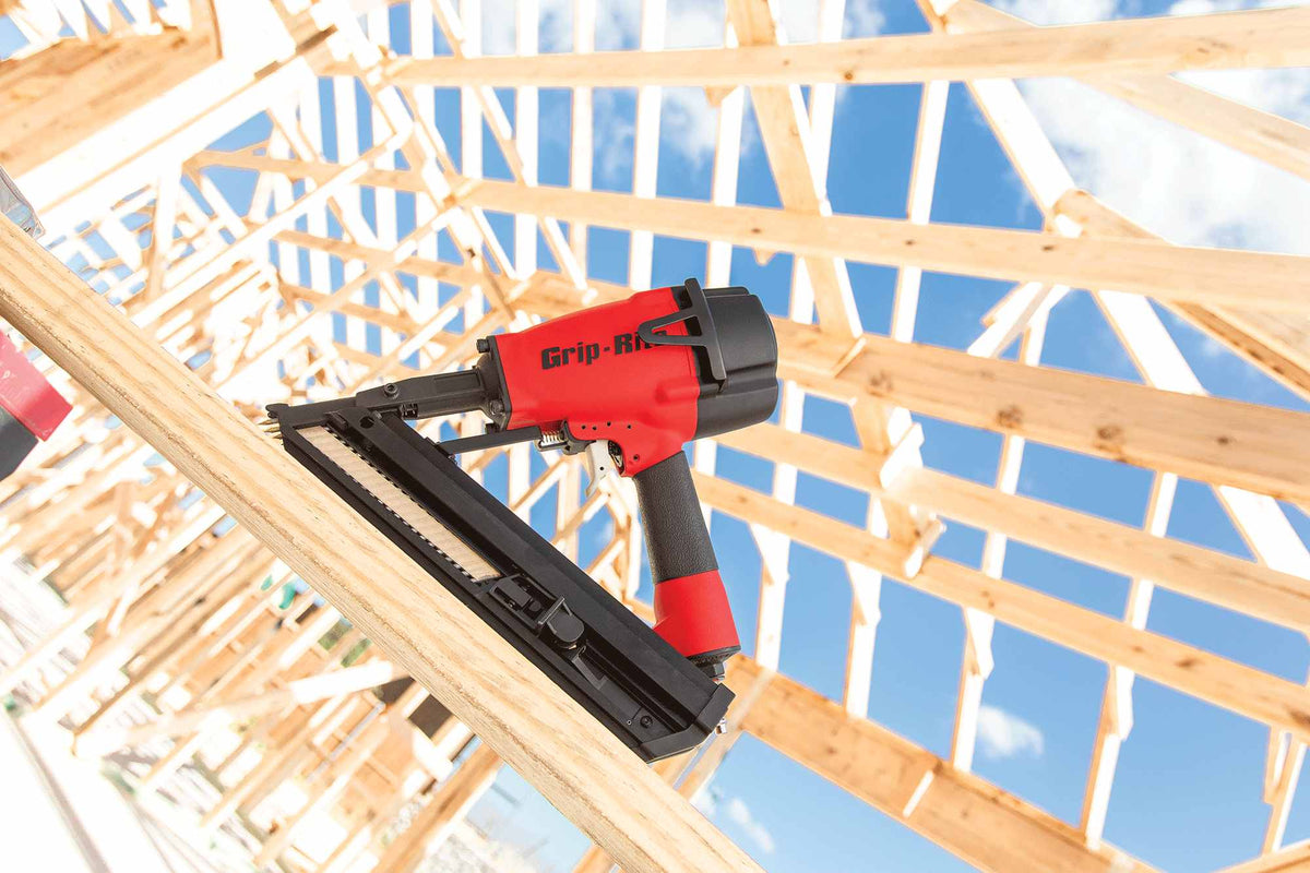 Professional jobsite application image showing the Grip Rite GRSB250 metal connector nailer resting on structural lumber during a residential framing project under a clear blue sky.