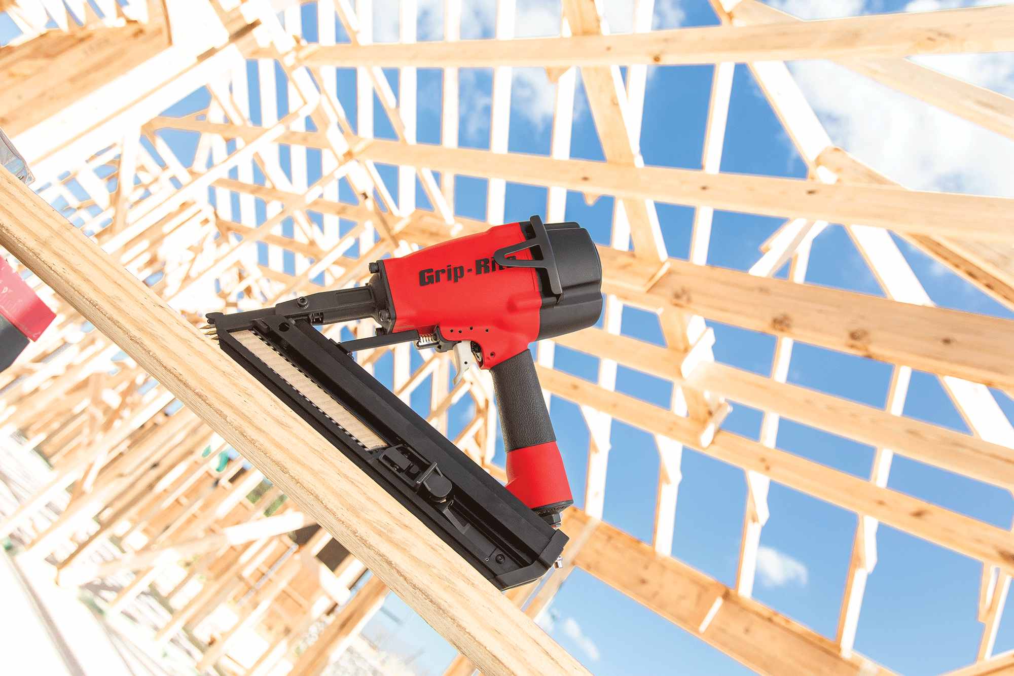 Professional jobsite application image showing the Grip Rite GRSB250 metal connector nailer resting on structural lumber during a residential framing project under a clear blue sky.