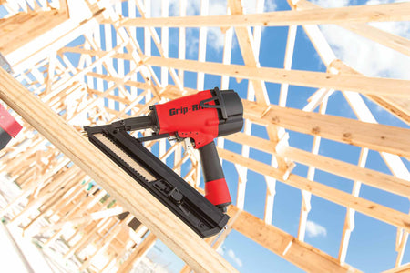 Professional jobsite application image showing the Grip Rite GRSB250 metal connector nailer resting on structural lumber during a residential framing project under a clear blue sky.