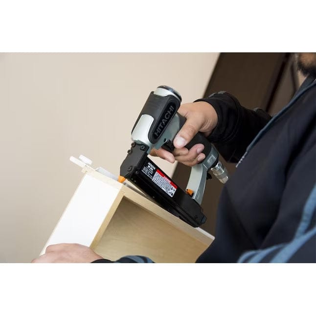 An action shot of a worker using the Hitachi NP35A pin nailer to fasten trim onto a white cabinet.