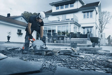  Construction worker using a large circular saw to cut concrete slabs at a residential jobsite with safety gear on.