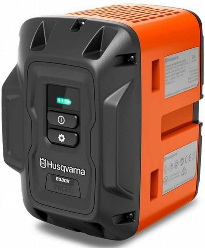 A detailed angled view of the Husqvarna B380X PACE battery, featuring its orange and dark gray casing, power indicator lights, and control buttons.