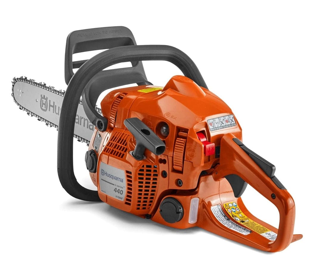 Close-up of Husqvarna 440 chainsaw with safety labels and pictograms, showing orange body, black handle, silver chain bar, and "PULL BACK TO KEEP" safety guard text.