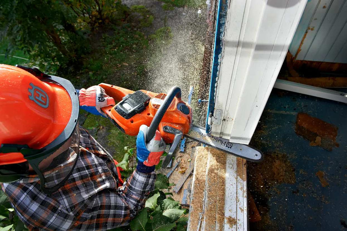 High-angle action shot of a professional contractor wearing a hard hat and safety gear using the Husqvarna 535i XP chainsaw to perform a precision cut on a wooden door frame.