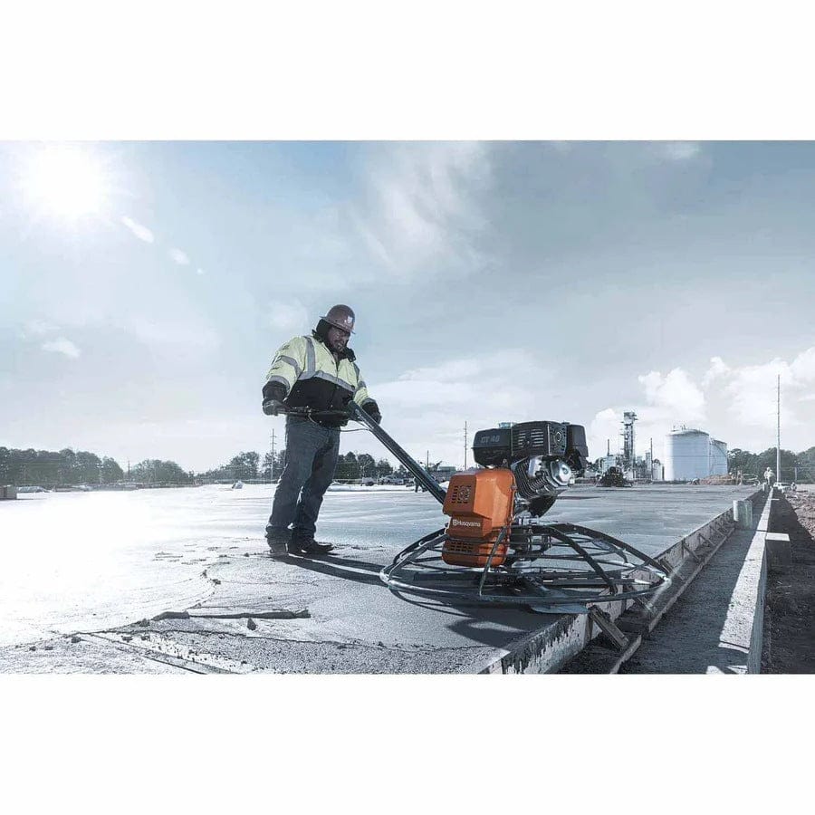 A professional contractor operating the Husqvarna CT 48 walk-behind power trowel on a large-scale industrial concrete pour, demonstrating the tool's effectiveness for high-production concrete finishing.