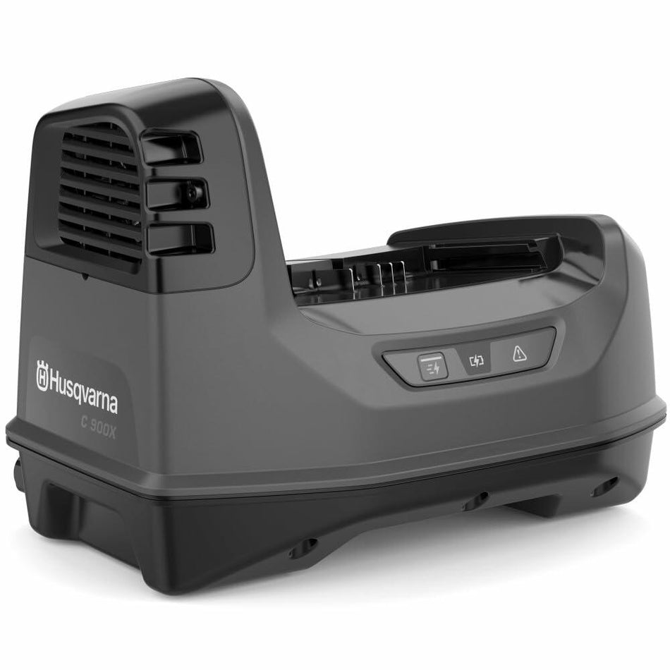 A three-quarter studio shot of the Husqvarna C900X PACE battery charger, showing its dark gray body, battery slot, control buttons, and the active cooling vent.