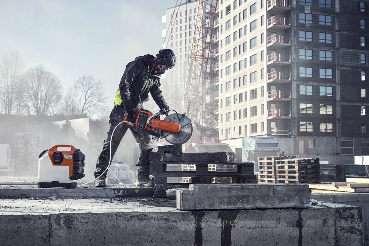 An operator on a construction site using the Husqvarna K1 PACE saw to cut concrete blocks while connected to the WT15i water tank for dust suppression.