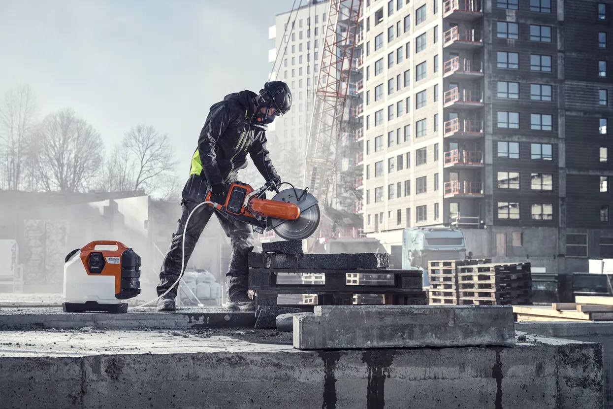 An operator on a construction site using the Husqvarna K1 PACE saw to cut concrete blocks while connected to the WT15i water tank for dust suppression.