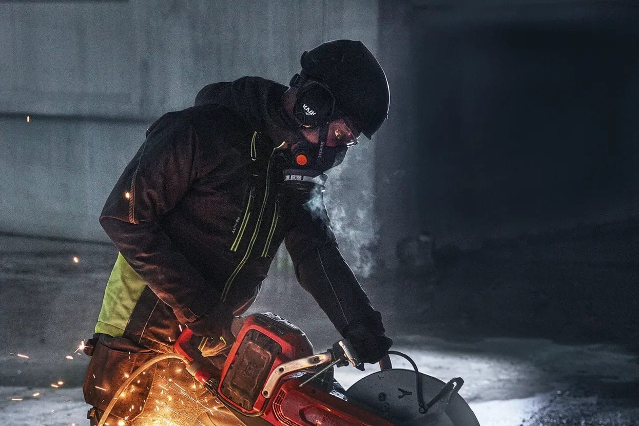 A professional operator wearing a respirator, helmet, and safety gear using the Husqvarna K1 PACE saw to cut through material, with sparks flying from the blade.