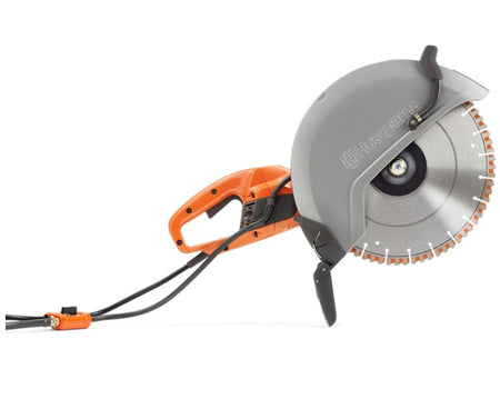 Angled view of the Husqvarna K4000 electric power cutter, focusing on the large gray blade guard and the long orange power cord connected to a water control valve.